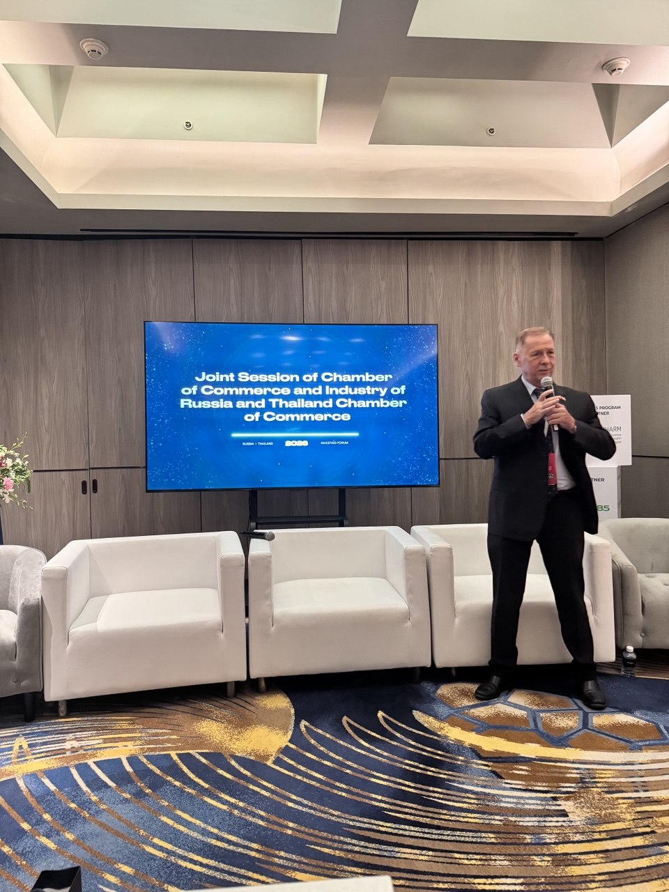 Vitaly Kiselev speaking beside the joint chamber session screen at RTIF 2026 in Bangkok.
