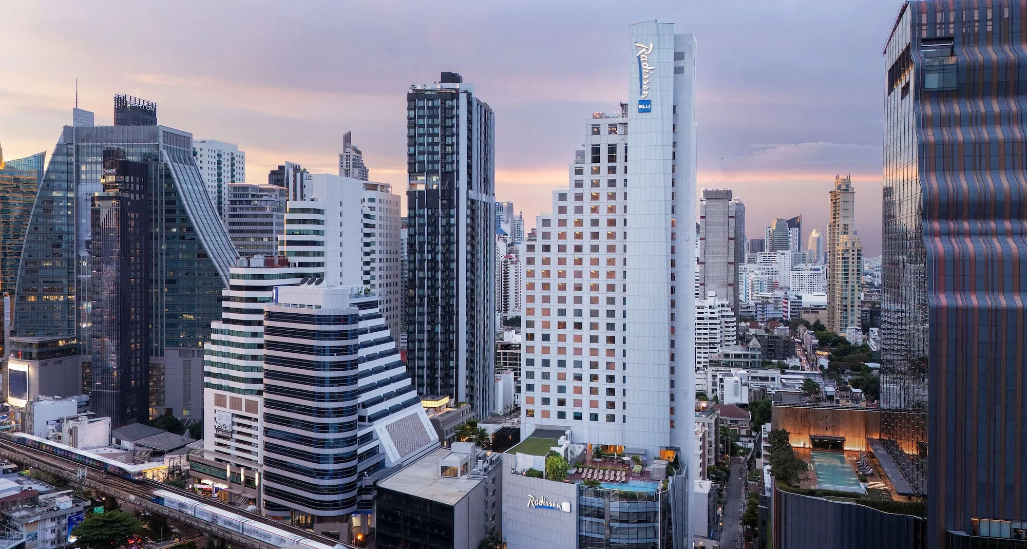Exterior view of Radisson Blu Plaza Hotel, Bangkok, surrounded by the Sukhumvit skyline at dusk.