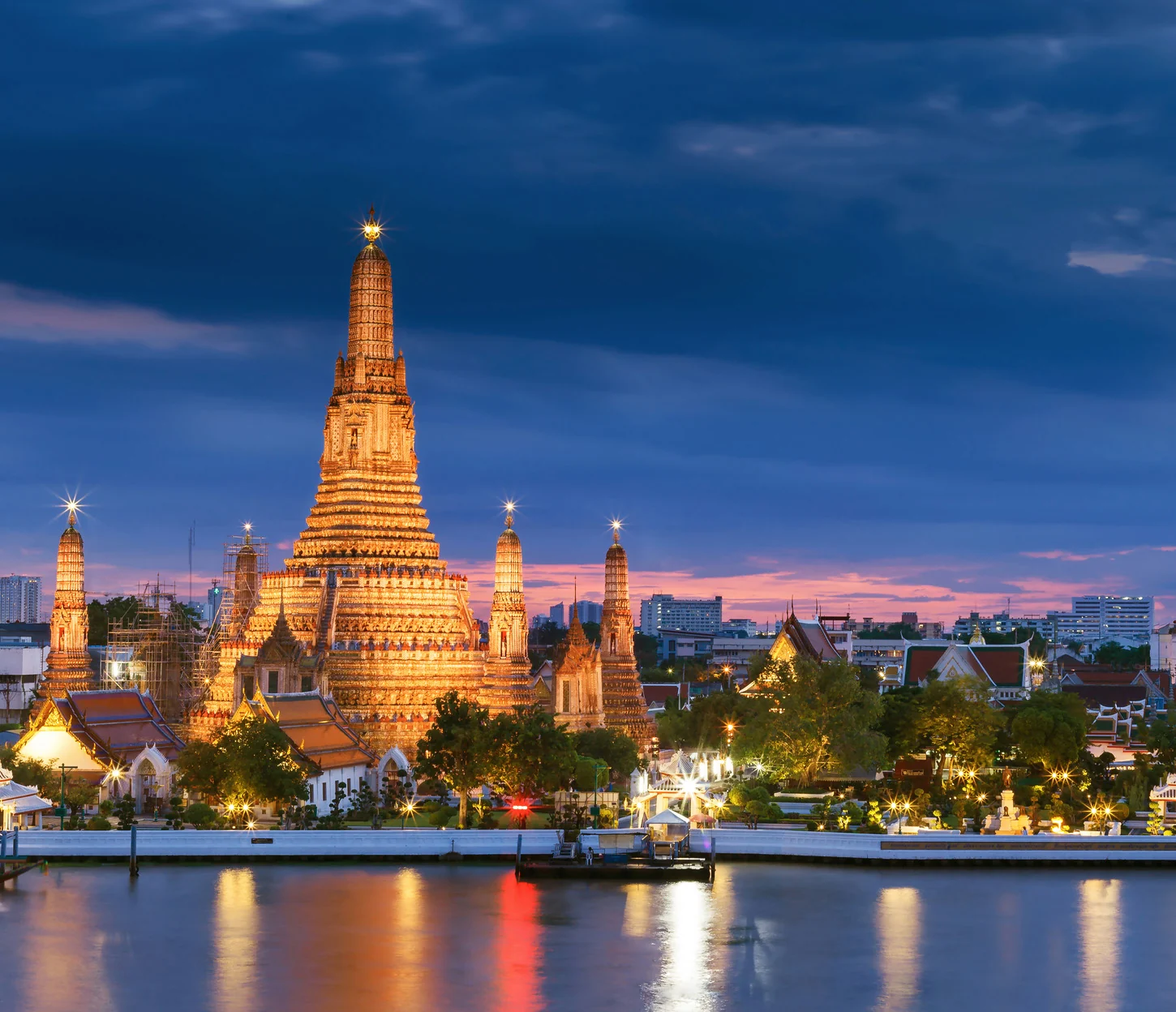 Wat Arun illuminated beside the Chao Phraya River in Bangkok at dusk