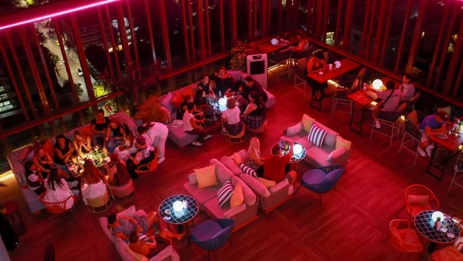 Guests in lounge seating on Mimi’s rooftop terrace at night under pink and red lighting