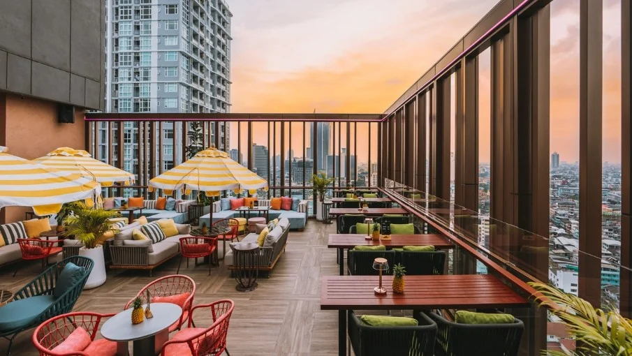 Mimi’s rooftop terrace at sunset with parasols, lounge seating and the Bangkok skyline